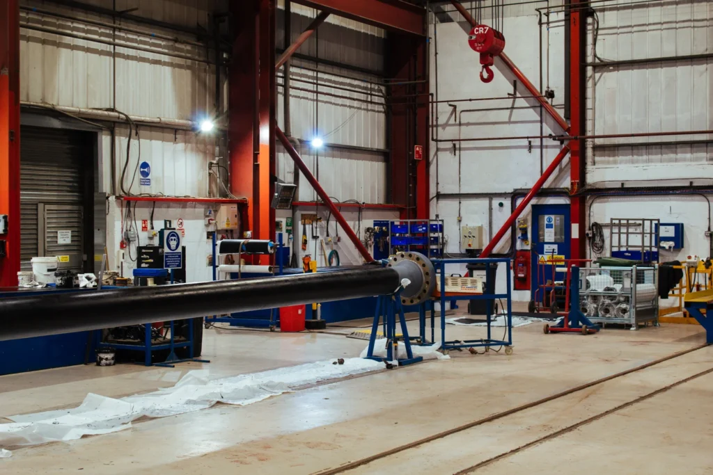 Black-coated steel pipe with flange end positioned in LJF Custom Coatings workshop for quality inspection