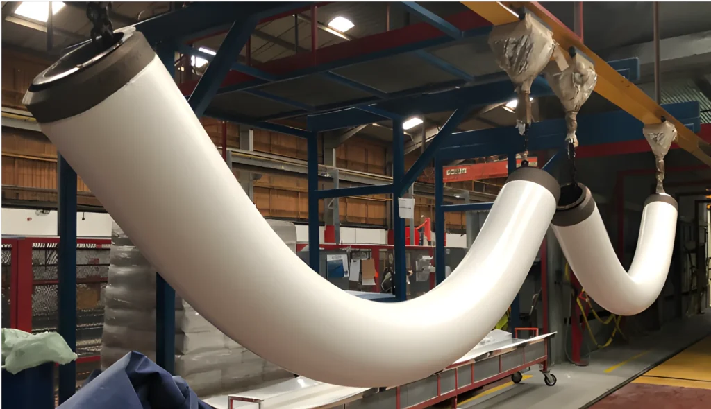 Curved steel pipes with white protective coating suspended for curing at LJF Custom Coatings facility