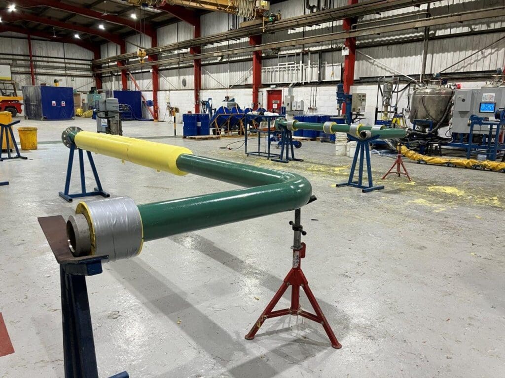 Multiple coated pipe spools including green-coated bends and yellow PU-insulated sections inside LJF Custom Coatings workshop