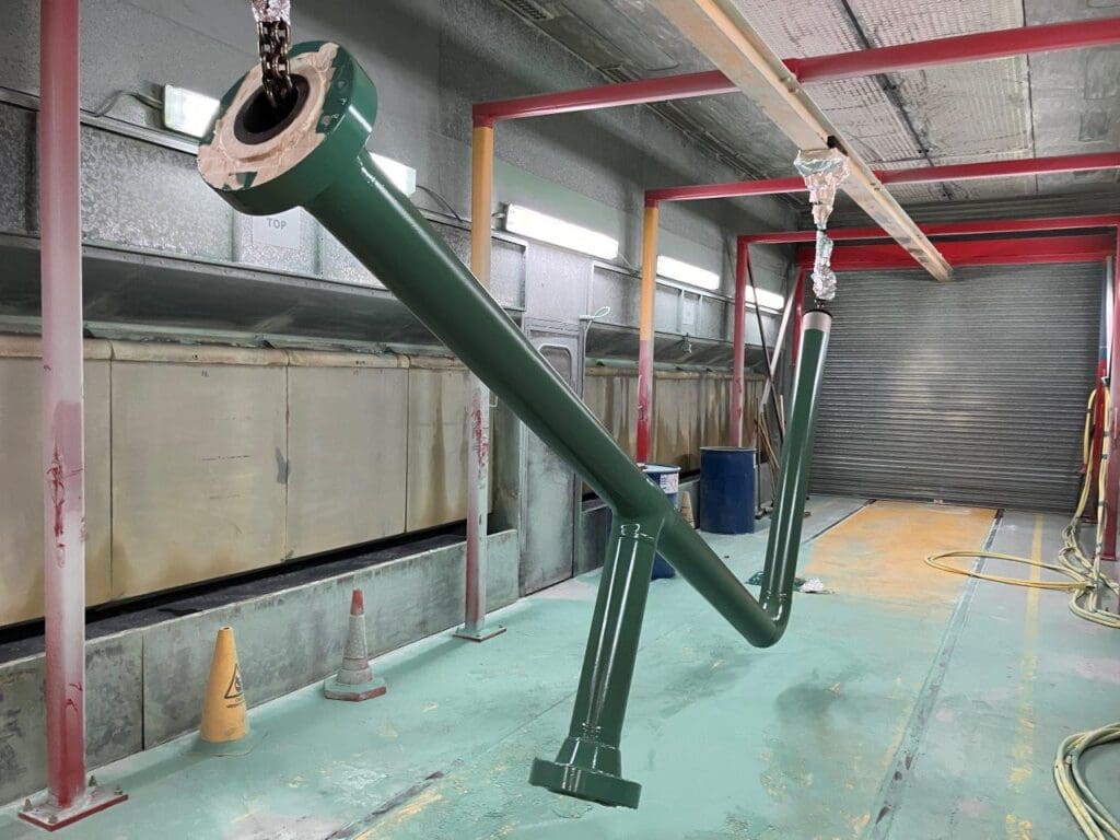 Green-coated subsea pipe with flanged ends suspended in LJF Custom Coatings spray booth
