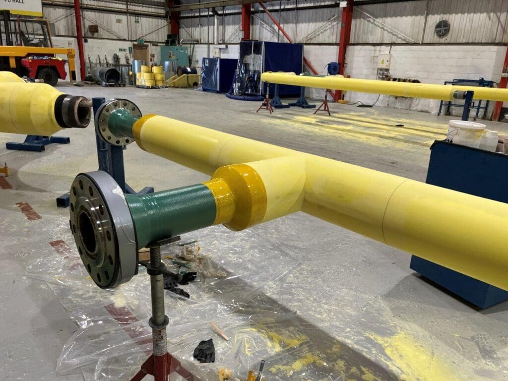 T-shaped pipe spool with yellow polyurethane insulation and green flanged branch outlet at LJF Custom Coatings facility