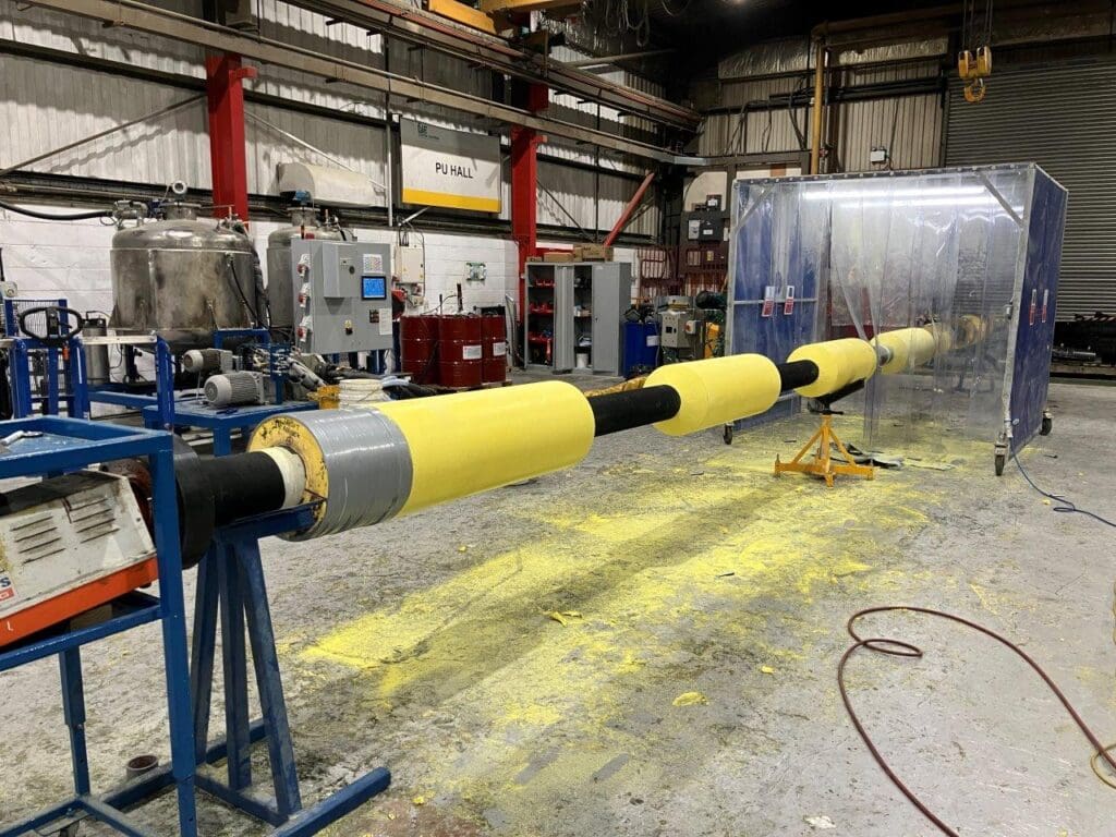 Pipeline undergoing solid polyurethane insulation process in LJF Custom Coatings’ PU Hall, with machinery and yellow PU layers visible