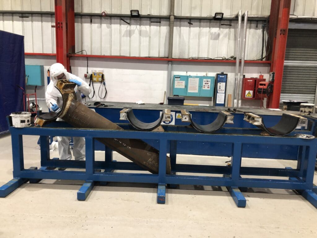 Technician in white PPE working on a steel clamp assembly component at a workstation in LJF Custom Coatings facility
