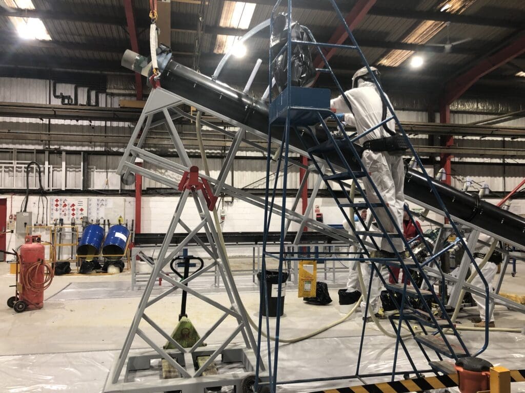 LJF Custom Coatings technicians preparing coated pipework in workshop with overhead crane and support frame