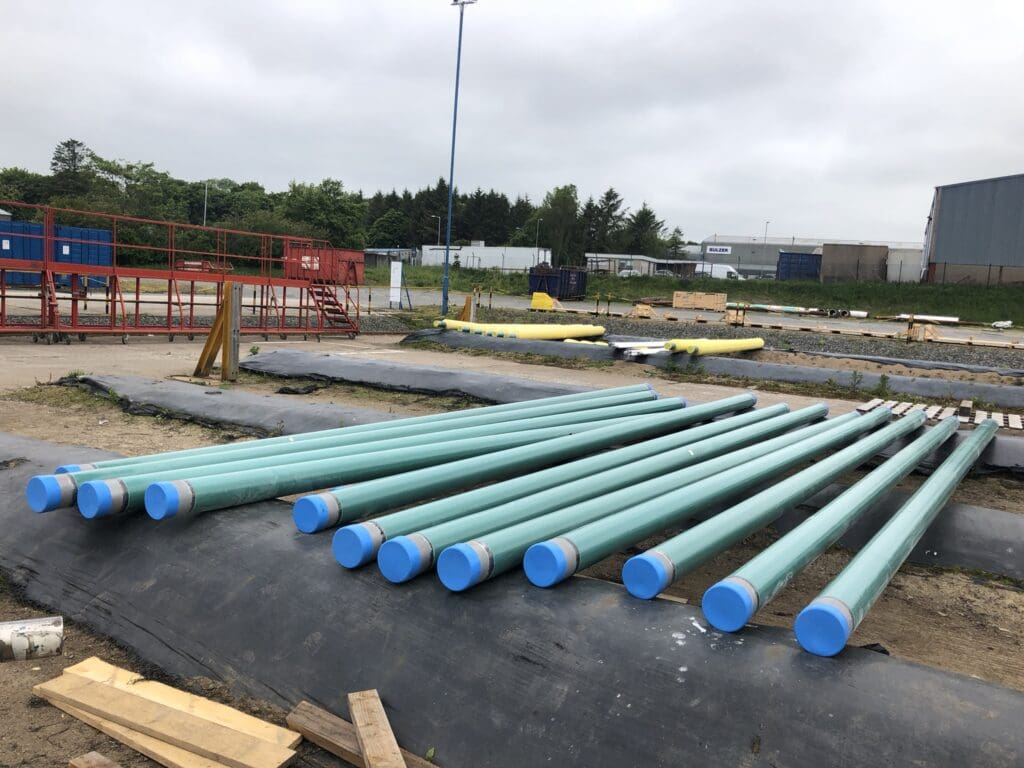 Fusion Bonded Epoxy (FBE) coated pipes with blue end caps stored outdoors at LJF Custom Coatings facility