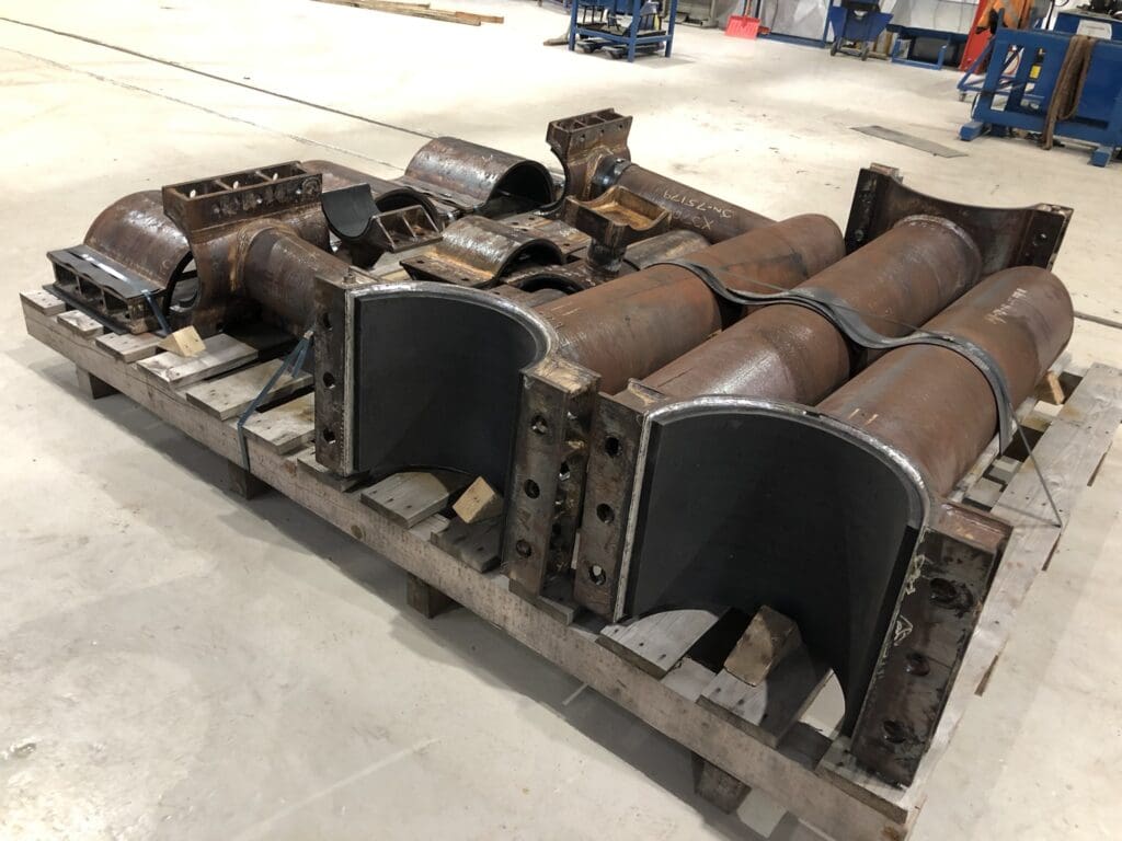 Steel clamp and half-shell components staged on a pallet in LJF Custom Coatings workshop, awaiting surface prep and coating