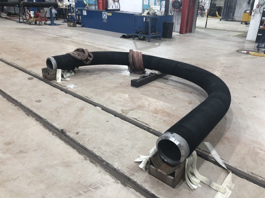 Large-radius subsea pipe bend with black Neoprene or EPDM coating staged for inspection at LJF Custom Coatings