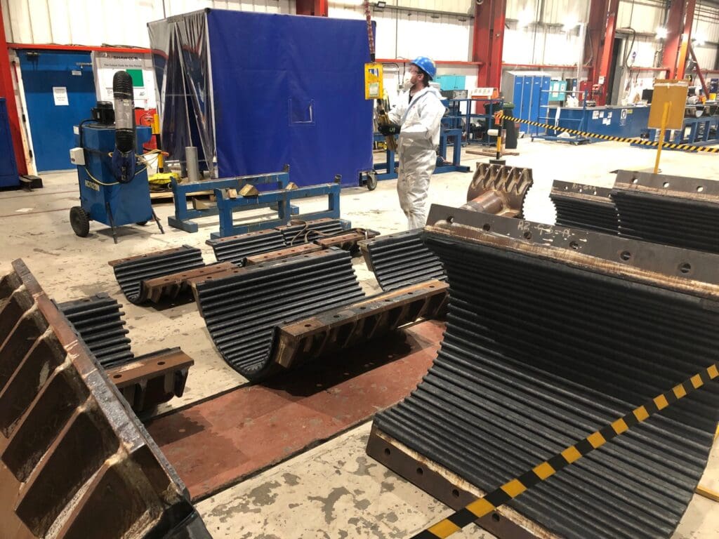Segmented buckle arrestor components with grooved interiors staged for preparation at LJF Custom Coatings workshop, with technician in PPE nearby