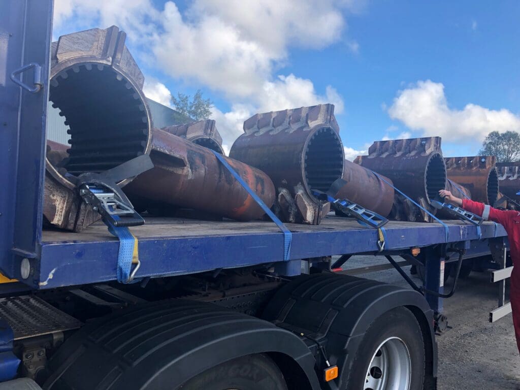 Uncoated buckle arrestor components with toothed ends secured on a flatbed trailer, prepared for coating or delivery at LJF Custom Coatings