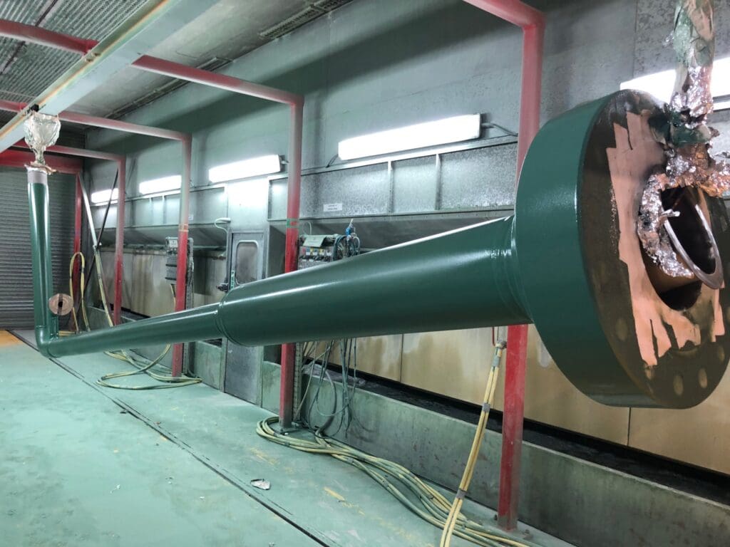 Green-coated steel spool with flanged ends hanging in LJF Custom Coatings facility for inspection