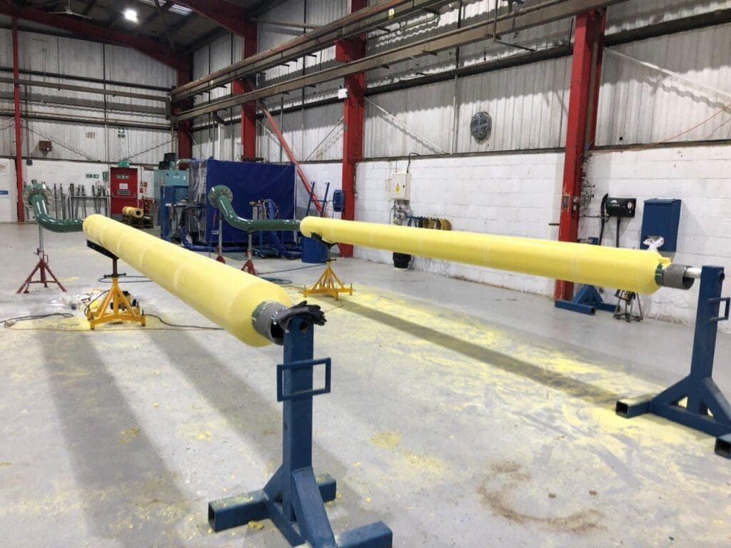 Long straight pipe spools with yellow PU thermal insulation staged on stands inside LJF Custom Coatings facility