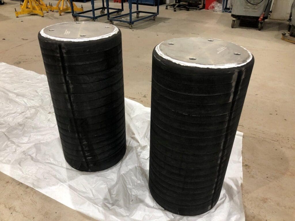 Two cylindrical components with black Neoprene or EPDM rubber coating and metal end plates, finished at LJF Custom Coatings