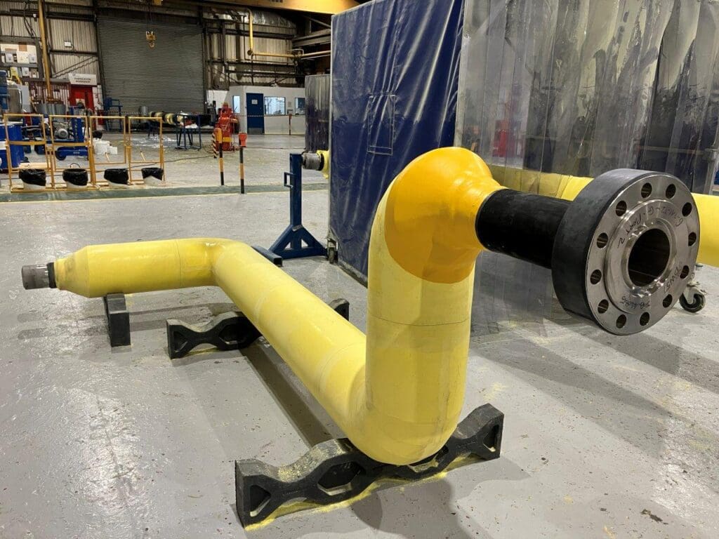 Yellow solid PU thermal insulation applied to a fabricated pipe spool with elbow and flange, inside LJF Custom Coatings facility